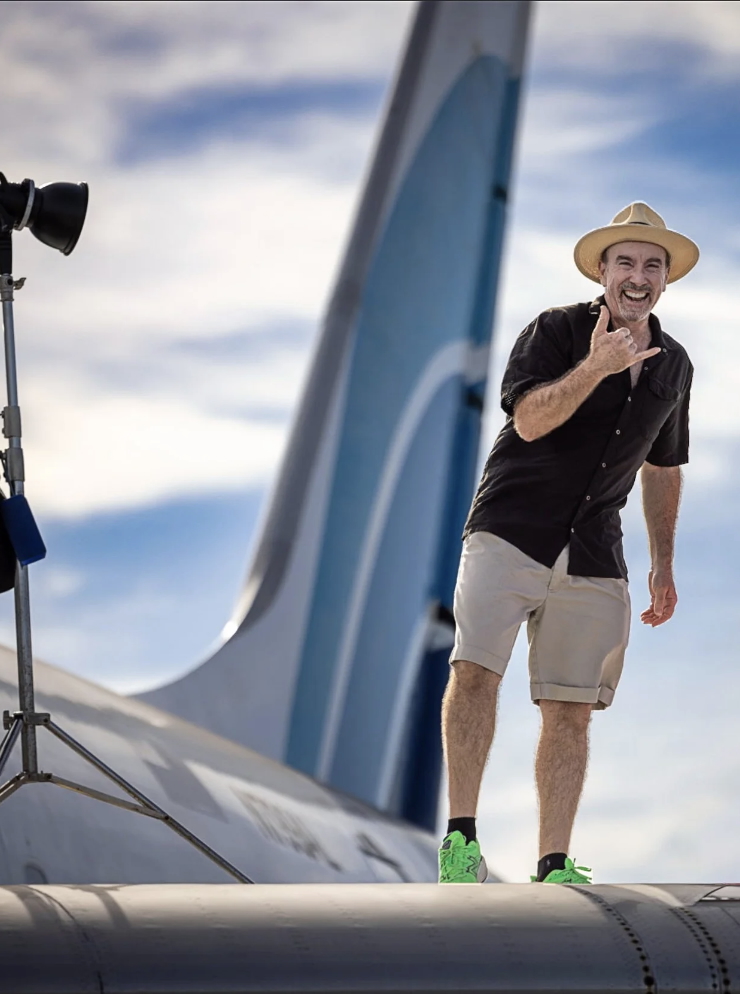 Laurence Balter laughing and giving a shaka sign, standing on the wing of a DC-8 beside a strobe light