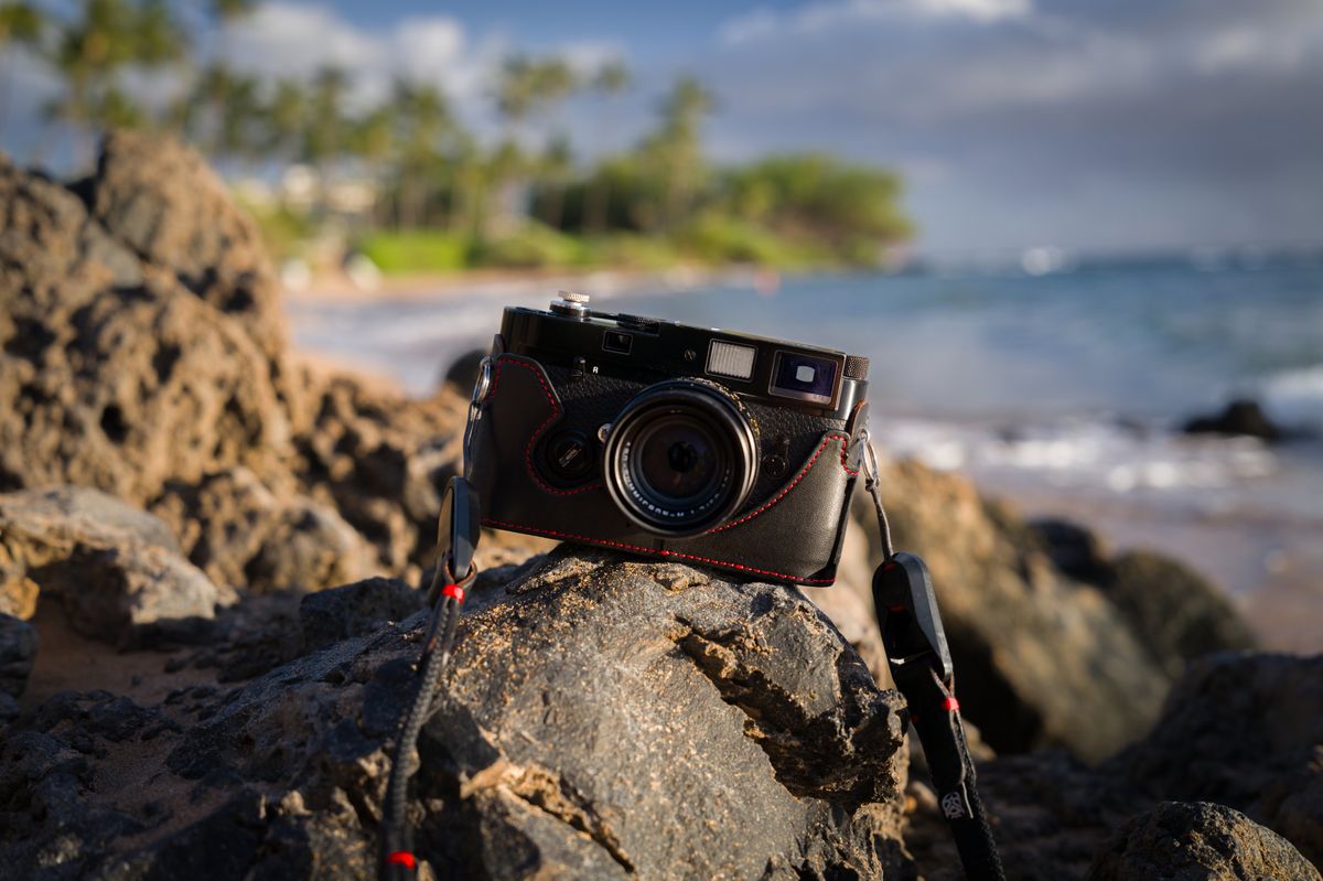 A Leica MP in a black leather Oberwerth half case with red stitching, on lava rock at a Maui beach