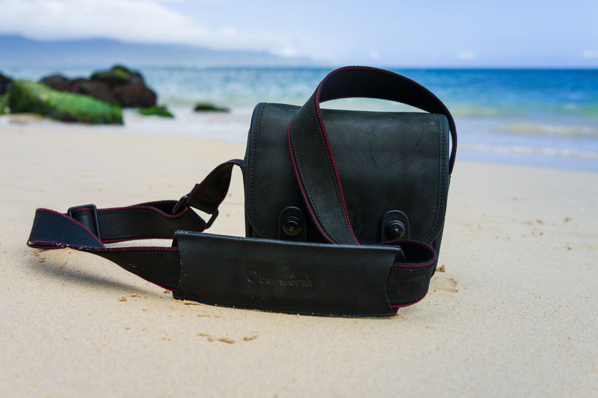 The Oberwerth Q Bag, a black leather camera bag with red stitching, on a Maui beach