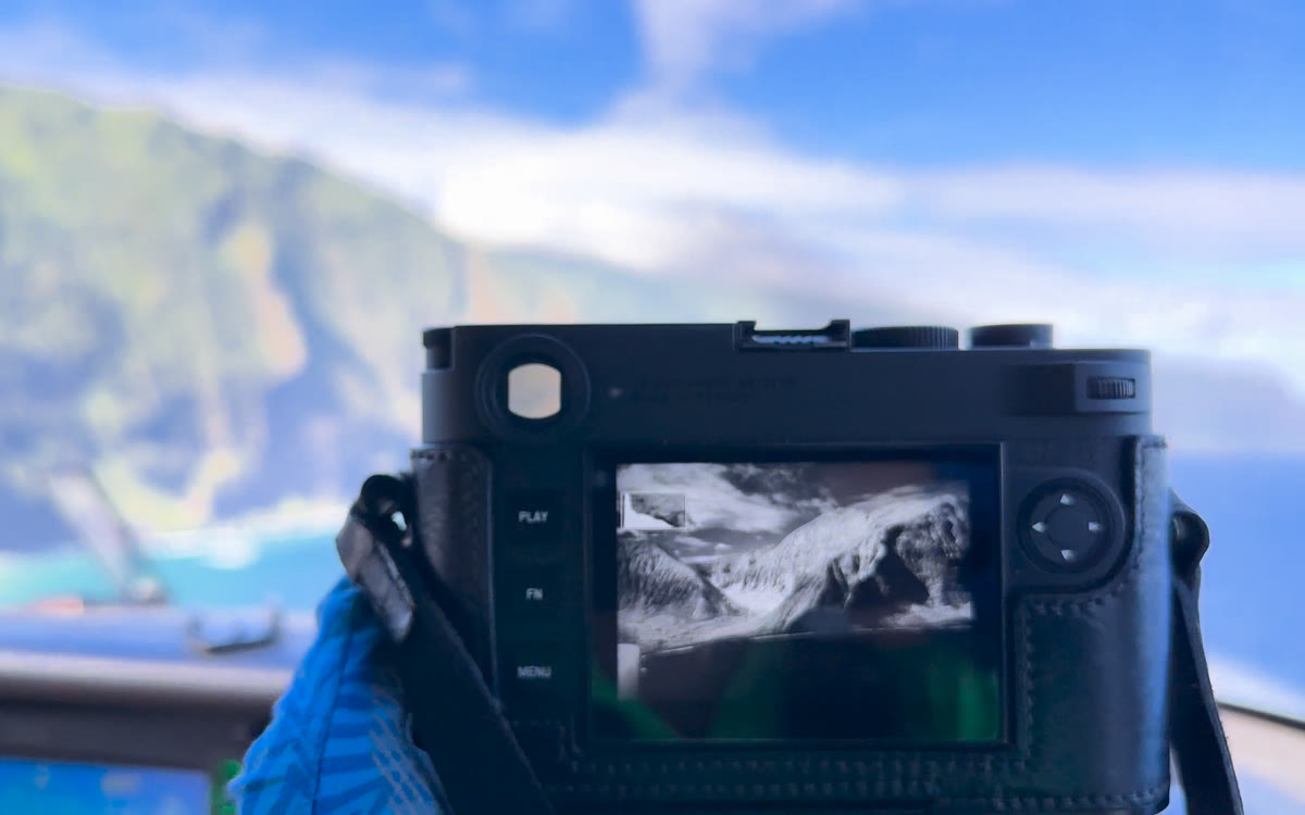 A Leica M11 Monochrom held in a cockpit showing a black-and-white image of Molokai on its screen