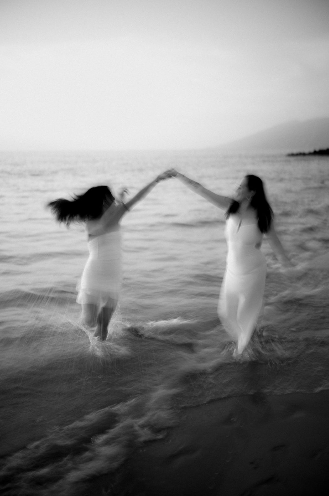 Black and white long exposure of two figures joining hands over the shallows