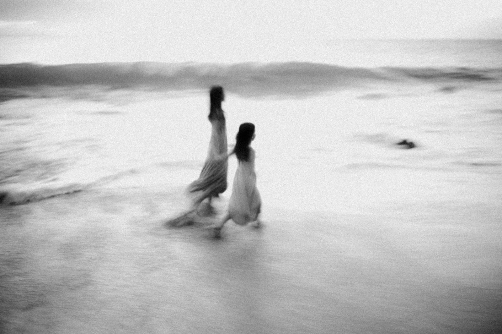 Black and white long exposure of two figures walking through shallow surf