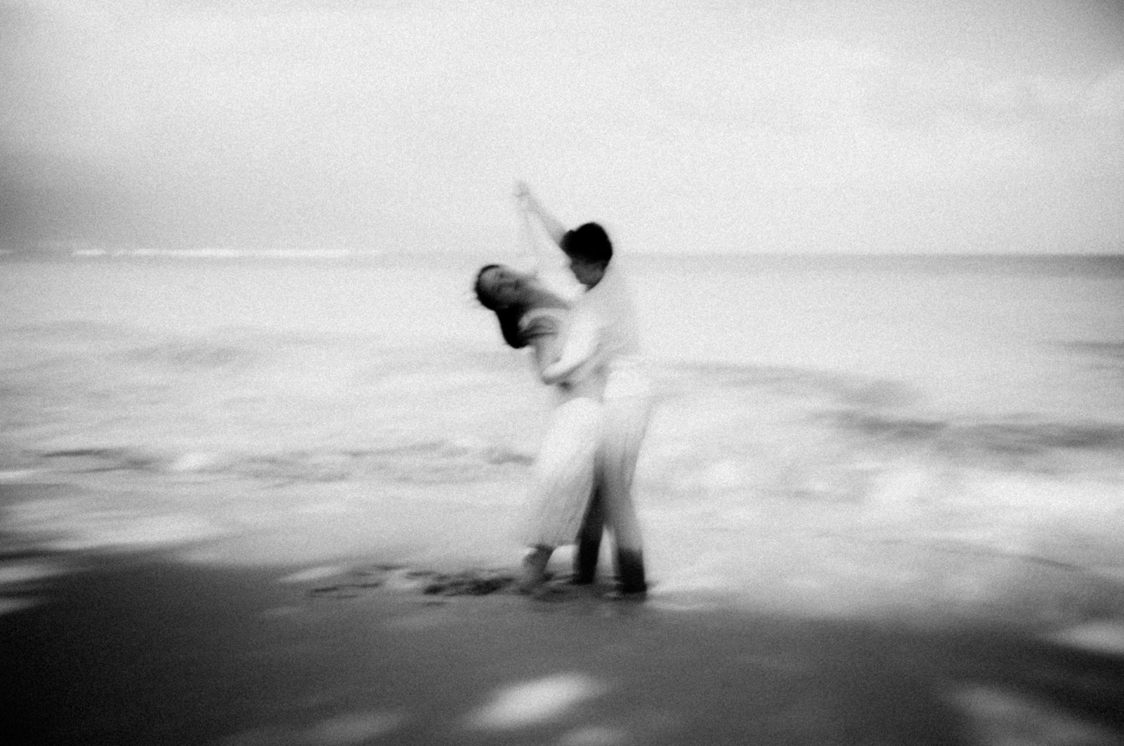 Black and white long exposure of a couple dancing at the water&rsquo;s edge