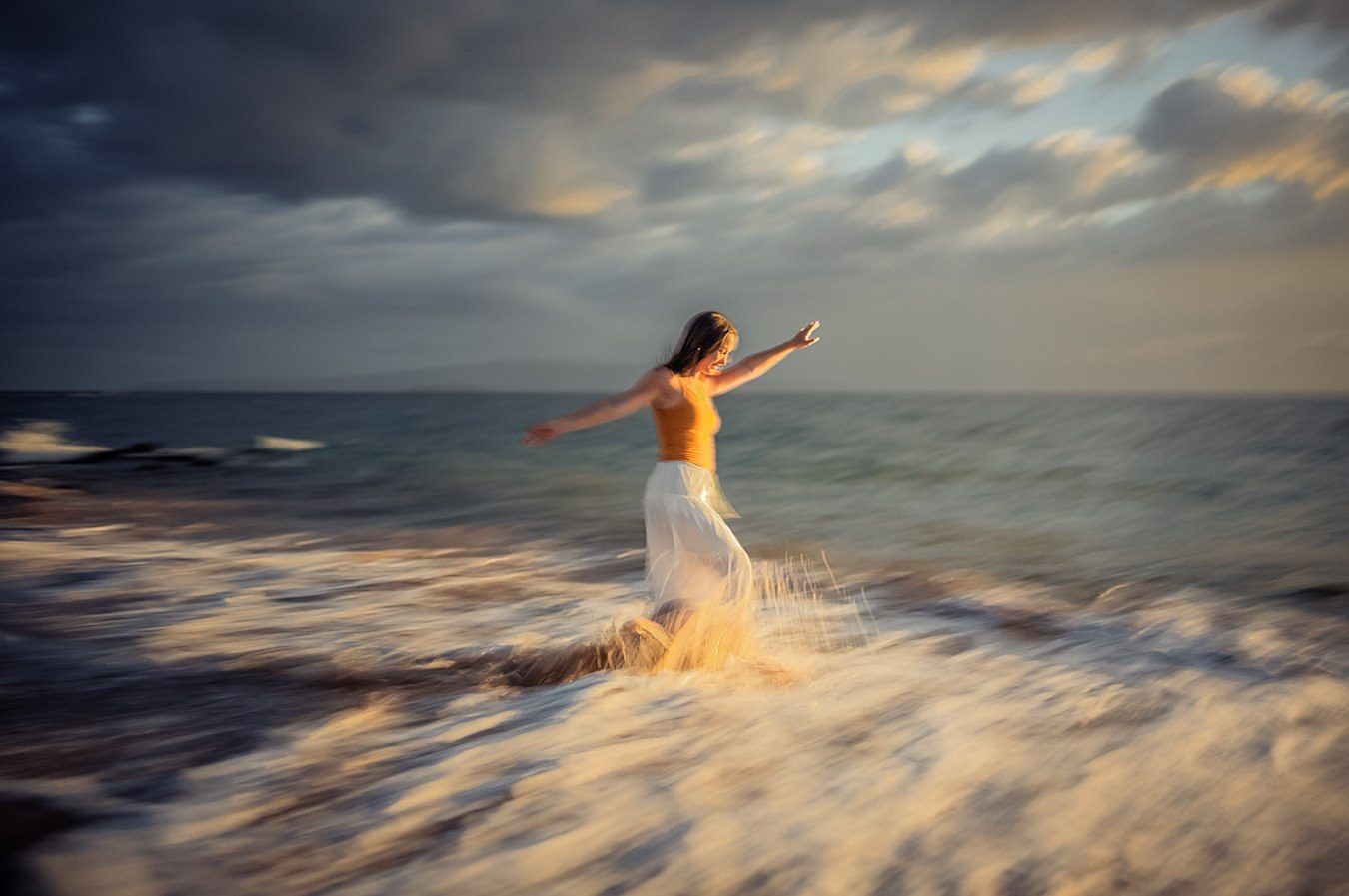 Color long exposure of a figure in an orange top with arms open, in the surf at dusk