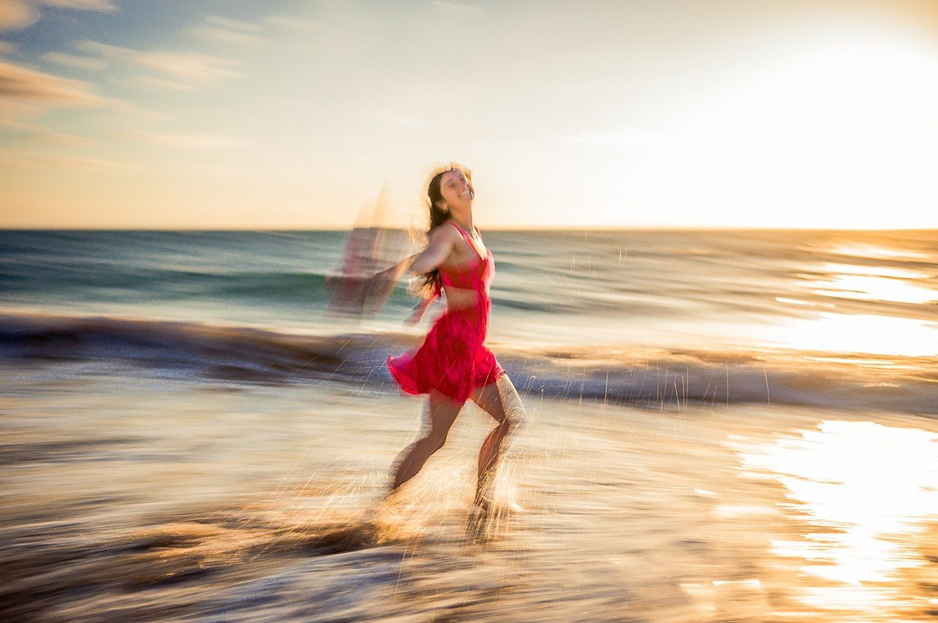 Color long exposure of a dancer in a red dress against golden sunlit water