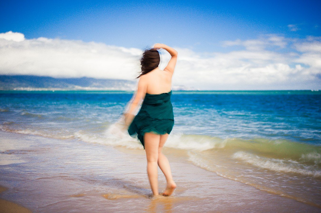 Color long exposure of a woman in a green dress seen from behind, facing a teal sea