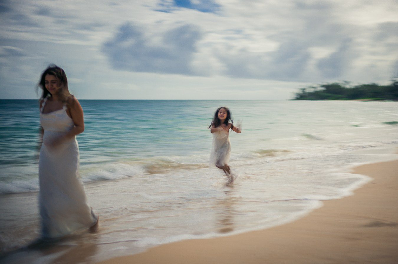 Color photograph of a woman and a girl in white dresses playing in the shallows