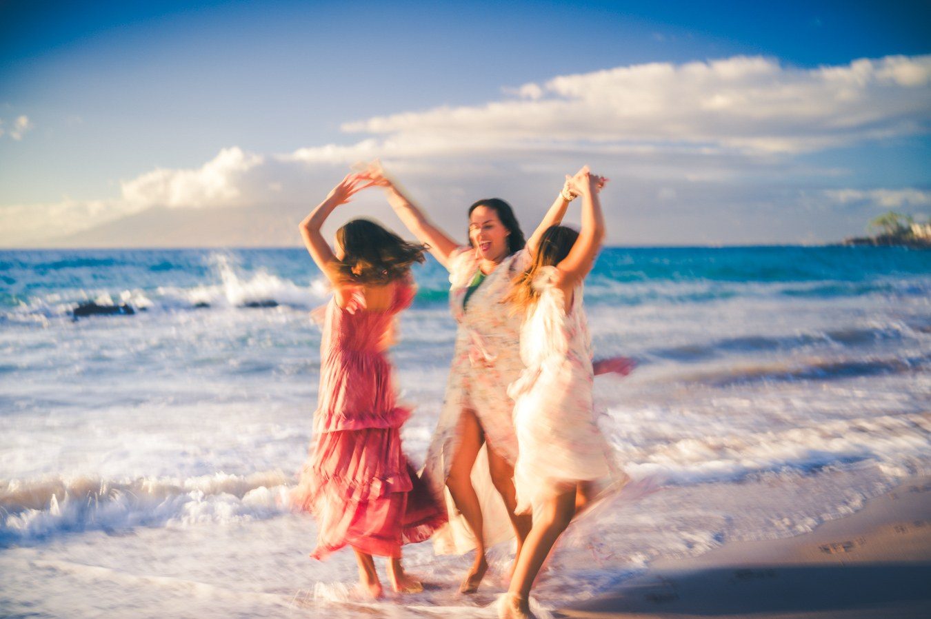 Color photograph of three women dancing in the surf under a blue evening sky