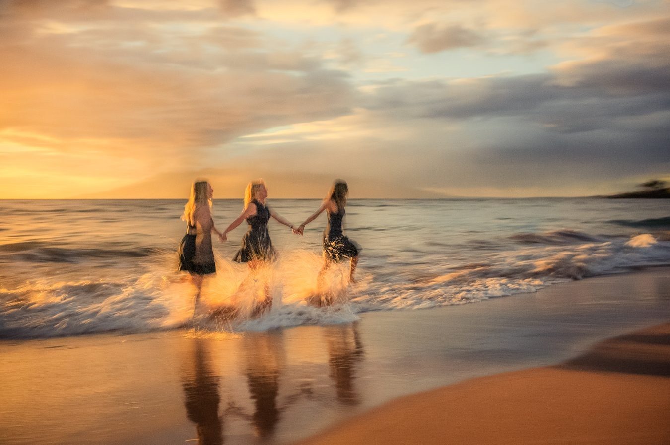 Color long exposure of three women holding hands and splashing through golden sunset surf